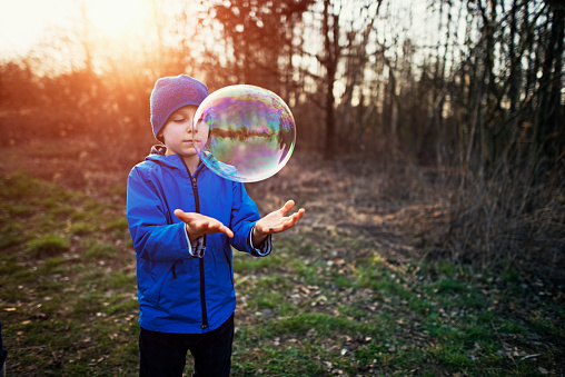 Little boy having fun with bubble in early spring. Cold and sunny spring day evening.\n