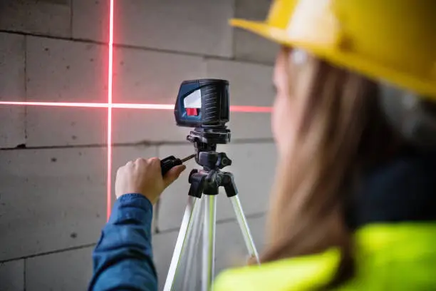 Female worker on the building site. Beautiful young woman with line laser level. House construction.