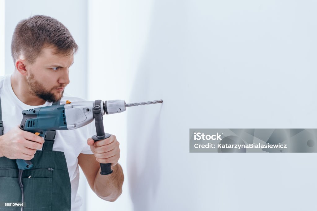 Male with a drill Handsome male with beard making a hole in white wall with a drill during interior finish Drill Stock Photo