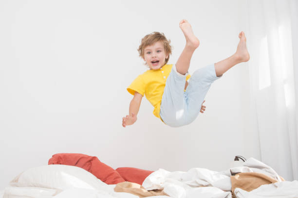 Cheerful little boy  jumping on bed at home stock photo