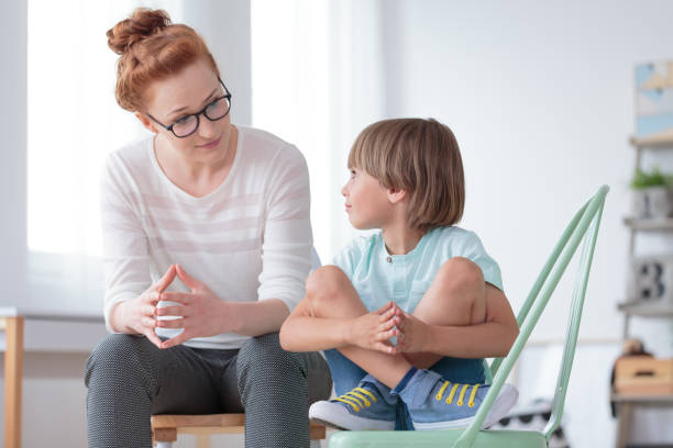 School psychologist with smart boy Young female school psychologist having serious conversation with smart little boy at office social services stock pictures, royalty-free photos & images