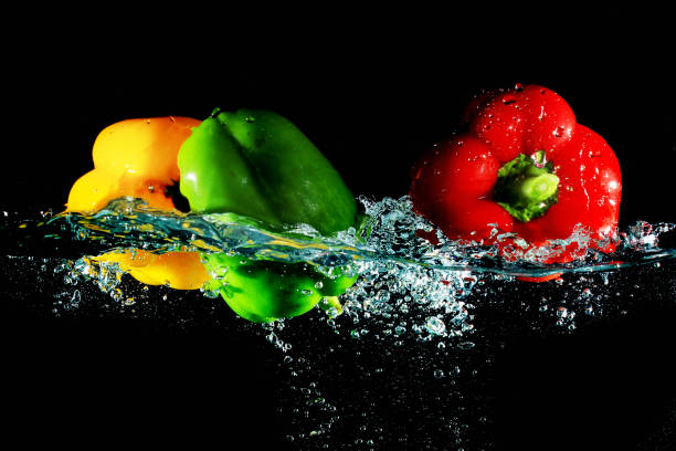 istock Red yellow and green peppers fall into water, on black background 888193498