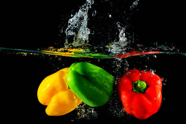 istock Red yellow and green peppers fall into water, on black background 888193532
