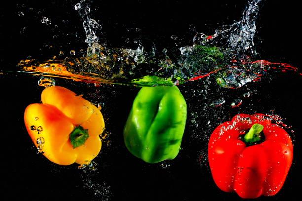 istock Red yellow and green peppers fall into water, on black background 888193628