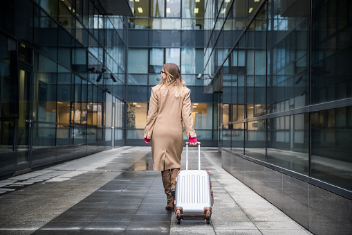 Young beautiful and stylish businesswoman pulling a suitcase and going on a business trip