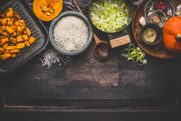 Pumpkin risotto cooking ingredients on dark rustic kitchen table with bowls, spoon and pan