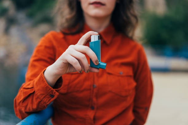 mujer joven con un inhalador de asma al aire libre - asthmatic fotografías e imágenes de stock