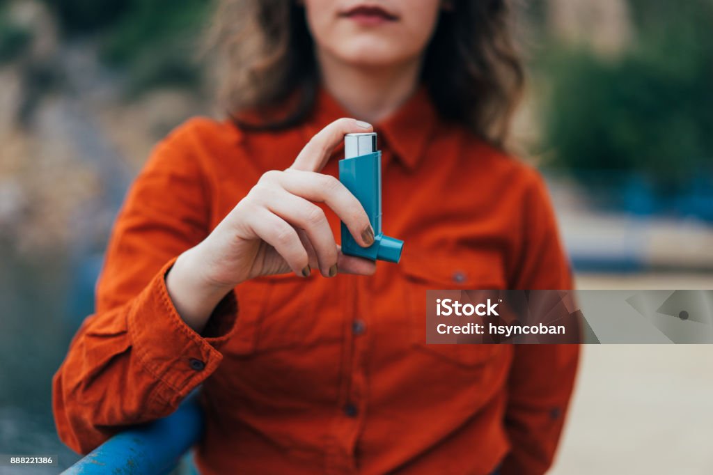 Young woman using an asthma inhaler outdoors Asthmatic Stock Photo