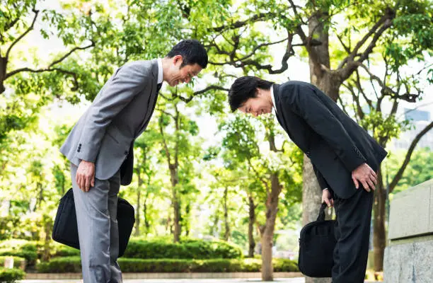 Two businessmen in Tokyo, dressed in suits, bowing to each other as a mark of respect.