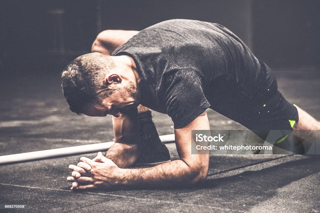 guy starts training preparation by doing streatching boy begins training preparation by streatching inside a gym, behind him the blackboard with workout points Cross Training Stock Photo