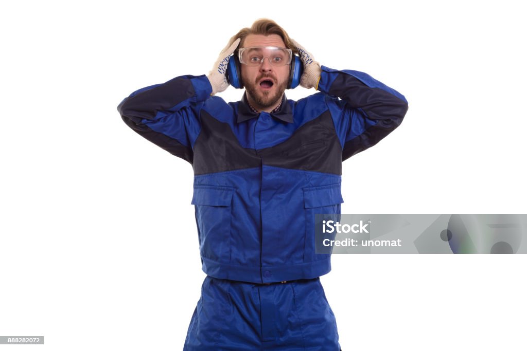 Surprised worker in safety glasses is standing with his mouth holding his headphones Surprised worker in safety glasses is standing with his mouth holding his headphones. Repairperson - Occupation Stock Photo