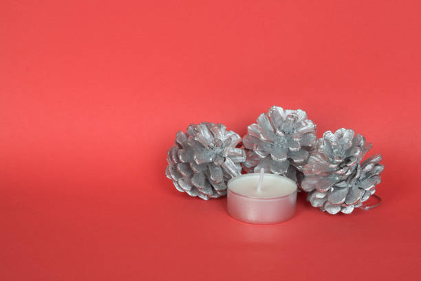 istock Silver painted pine cones with tea candle on red background. 888282546