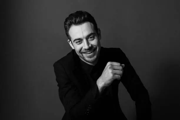 Black and white portrait of a young handsome man in a suit, smiling and looking at the camera, against plain studio background.