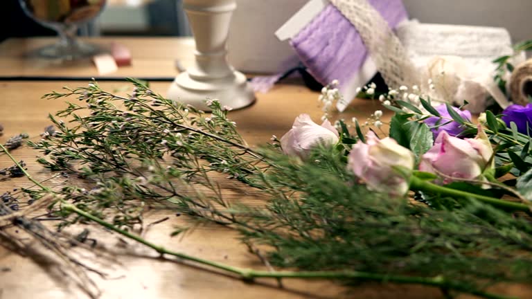 Slow camera movement showing wooden table with flowers, scissors, tapes, decorating paper and other tools for bouquet's arrangement at flower shop. Slowmotion shot