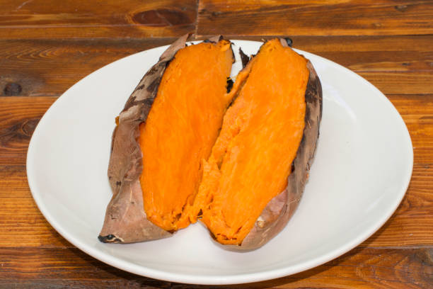 a sweet potato roasted A plate with a sweet potato roasted and opened in half, on a rustic wooden table bindweed photos stock pictures, royalty-free photos & images