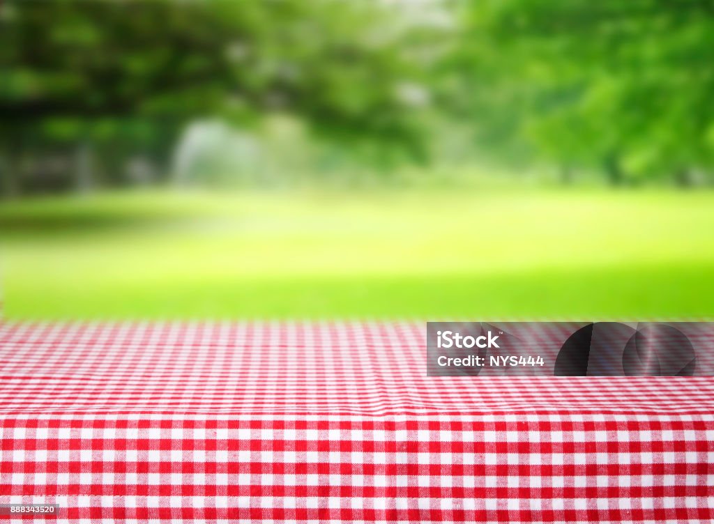 Checkered red tablecloth emty space table green background. Checkered red picnic tablecloth empty space table.Product display background. Picnic Stock Photo