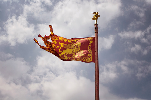 View of historical Venetian flag waving with cloudy sky background.