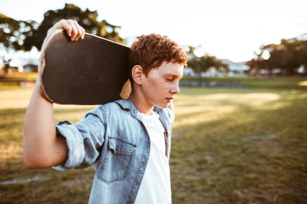 печальный ребенок со скейтбордом на плече - skateboard skateboarding outdoors sports equipment стоковые фото и изображения
