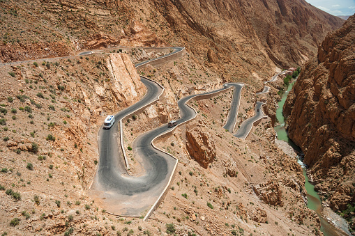 Morocco - Ouarzazate - Dades gorge - Steep mountain winding serpentine road with cars and rough river on the bottom of impressive gorge