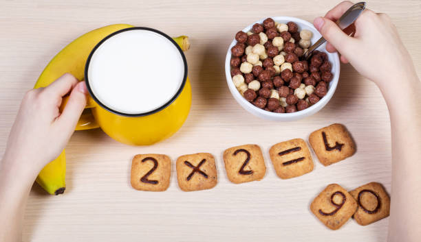 Healthy food for a school children. Milk, banana and funny cookies with numbers. Child has breakfast and does sums using biscuits. Idea of easy arithmetics during eating. stock photo