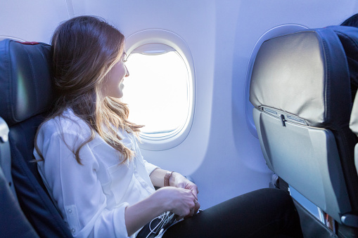 In this side view, a smiling young woman enjoys looking out the window of her aircraft as she awaits arrival to her destination.