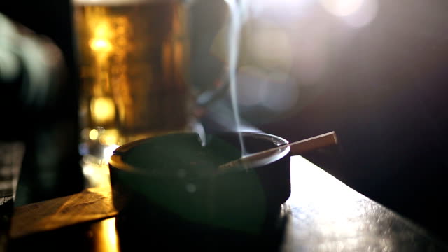 Cigarette in ashtray and glass of beer on the pub table