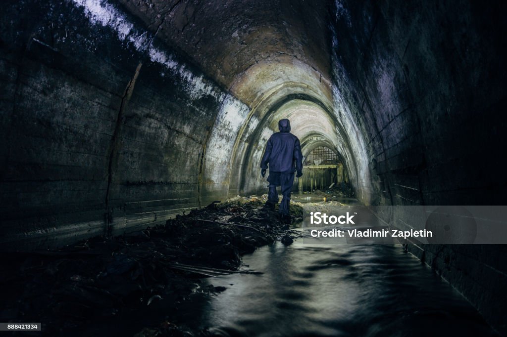 Sewer tunnel worker in chemical protective suite in underground gassy sewer tunnel Sewer tunnel worker in special chemical protective suite in underground gassy sewer tunnel Sewage Stock Photo