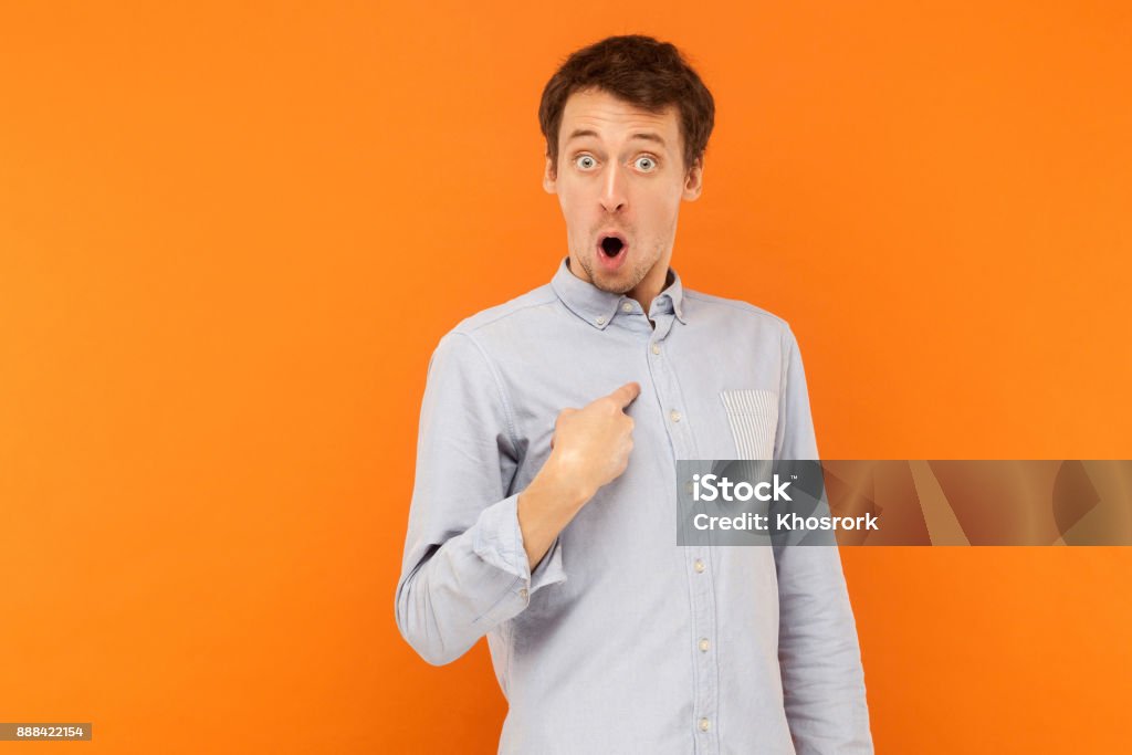 Who, i'm? Shocked man looking at camera and pointing finger himself Who, i'm? Shocked man looking at camera and pointing finger himself. Studio shot, orange background Pointing Stock Photo