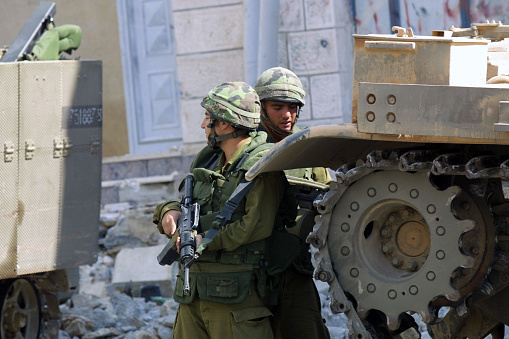 Hebron, Palestine - Oct. 5, 2001: Two Israeli soldiers stand between two armored vehicles guarding a street in the Palestinian part of the city.  Hebron, with a large Palestinian population and a small, but fervent, Jewish contingent, has historically been a flash point in the Israeli - Palestinian conflict.