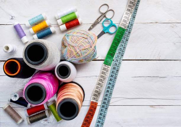 coloré bobines de ligne de fil à coudre, ciseaux, petits et grands et mètre-ruban sur le dessus de table de fond en bois blanc, un concept et une idée - sewing item photos et images de collection