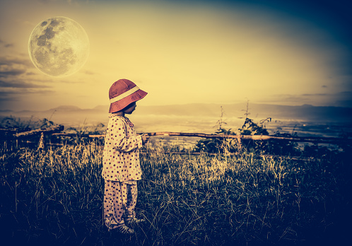 Asian child relaxing outdoors with bright full moon at night, travel on vacation. Adorable girl in night sky under beautiful full moon. Vintage tone effect. The moon were NOT furnished by NASA.