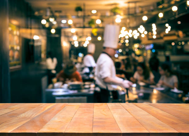 Wood table top with blur chef cooking in bar restaurant Wood table top with blur chef cooking in bar restaurant background.For create product display or design key visual layout busy restaurant tables stock pictures, royalty-free photos & images