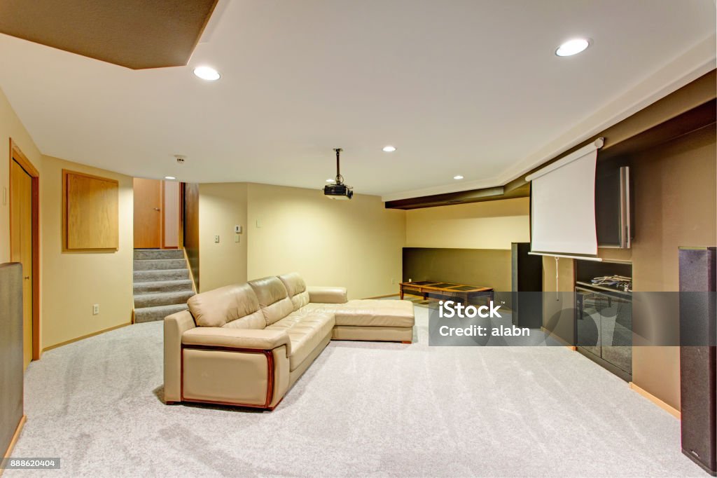 Beige basement movie room with a leather sectional Beige basement movie room features a leather sectional under a ceiling mounted movie projector. Basement Stock Photo