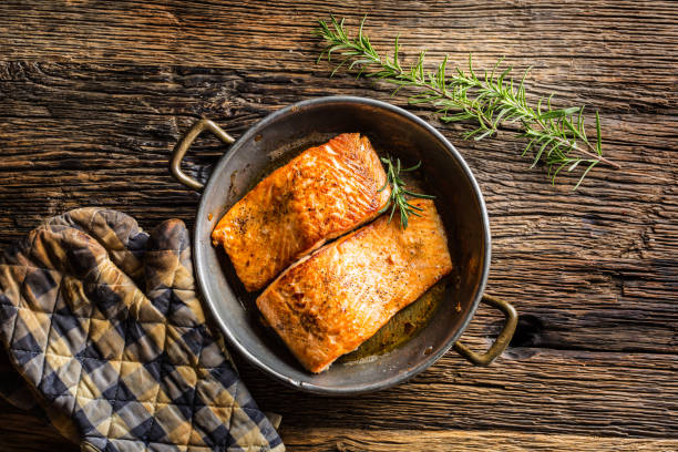 istock Salmon. Two juicy salmon steaks in roast pan with herb decoration on rustic oak table 888647526