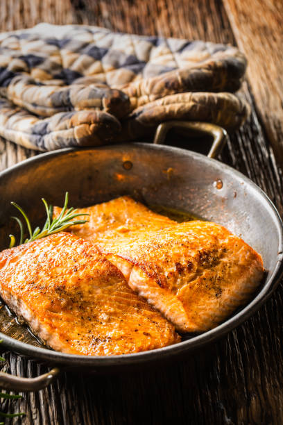 istock Salmon. Two juicy salmon steaks in roast pan with herb decoration on rustic oak table 888647530