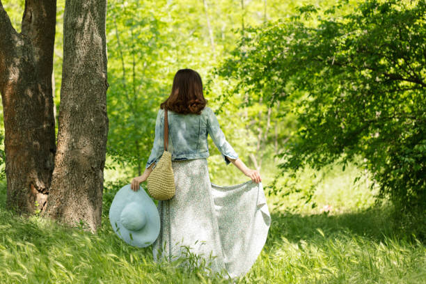 la giovane donna cammina in un parco con cappello e una gonna lunga con stampa floreale. - skirt women jeans white foto e immagini stock