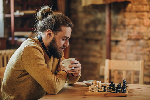 Pensive man sitting in a cafe and playing chess alone.