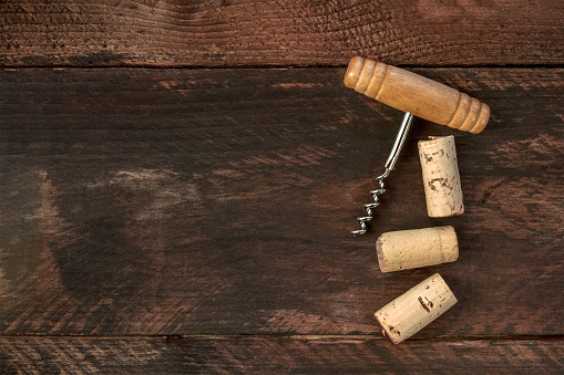 A photo of an old-fashioned corkscrew with corks, shot from above on a dark wooden background texture with a place for text. A design template for a wine list or a tasting invitation