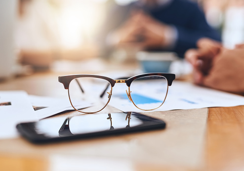 Closeup of a pair of reading glasses on a wooden table outside in a coffeeshop