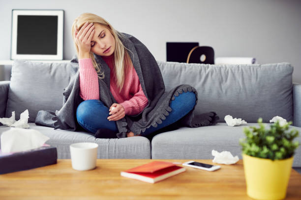 Sick woman with headache sitting under the blanket in living room stock photo