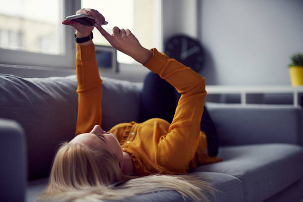 navegar por internet en su smartphone tumbado en el sofá en casa de la mujer - lying down women laptop freedom fotografías e imágenes de stock