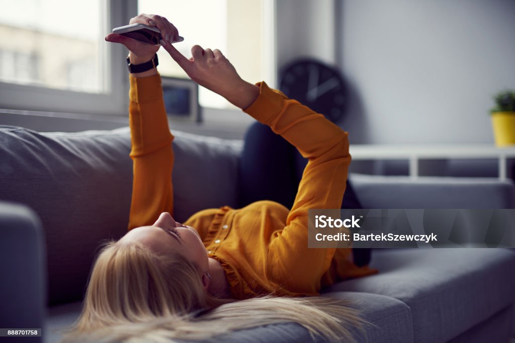 Woman browsing internet on her smartphone lying on the sofa at home Effortless Stock Photo