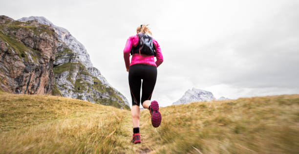 istock Woman running across grassy mountain ridge in high mountain range 888739290