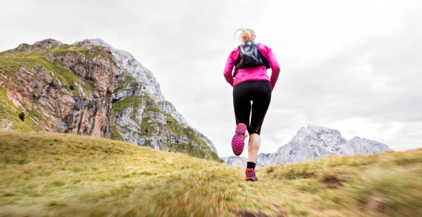 istock Woman running across grassy mountain ridge in high mountain range 888739310