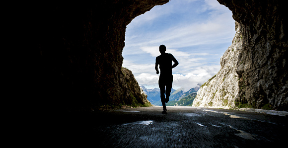 Male athlete running through tunnel in high mountain range on sunny day