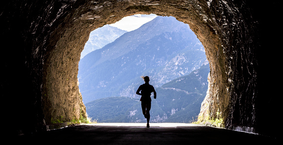 Female runner running through tunnel high in mountains.