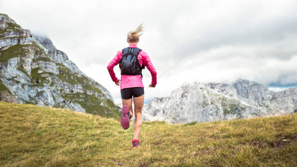 athlète féminine courir sur une pente herbeuse - cross coat photos et images de collection