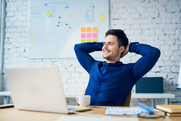 hombre joven satisfecho en la oficina mirando lejos - businessman happiness carefree computer fotografías e imágenes de stock