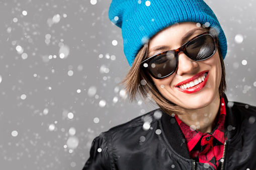 Young beautiful happy smiling girl over snowfall. Model wearing stylish outfit, closeup. empty space for text