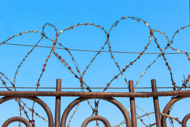 istock Barbed wire on a fence against the blue sky. 888756434